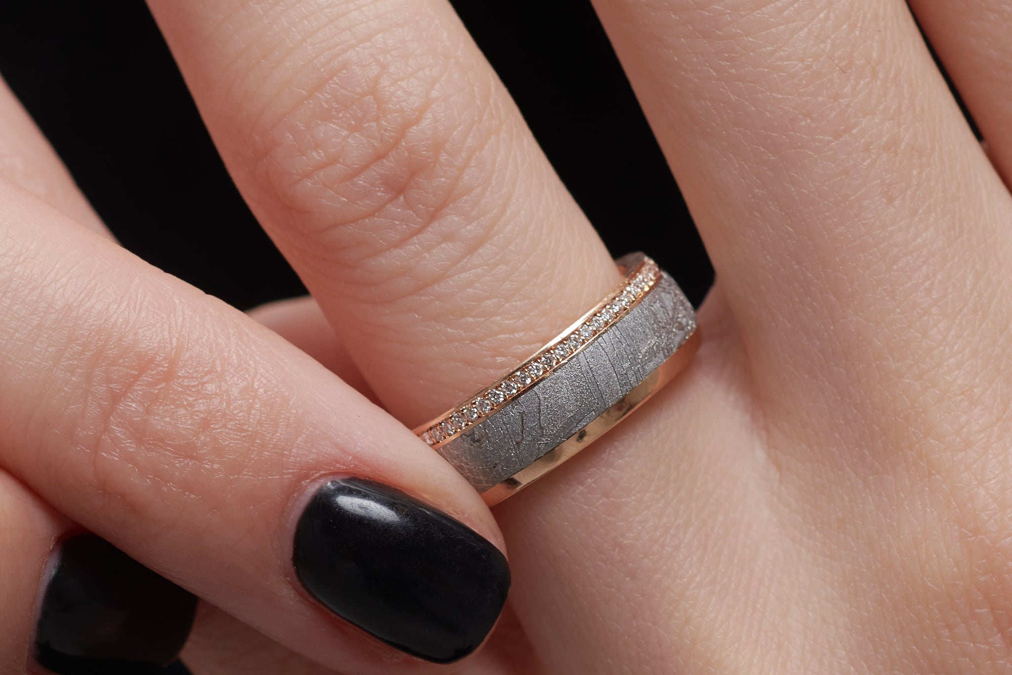 Eine Frau, die sich den Meteoriten Ring, der seitlich ein brillant besetztes Band hat, an den Finger steckt.