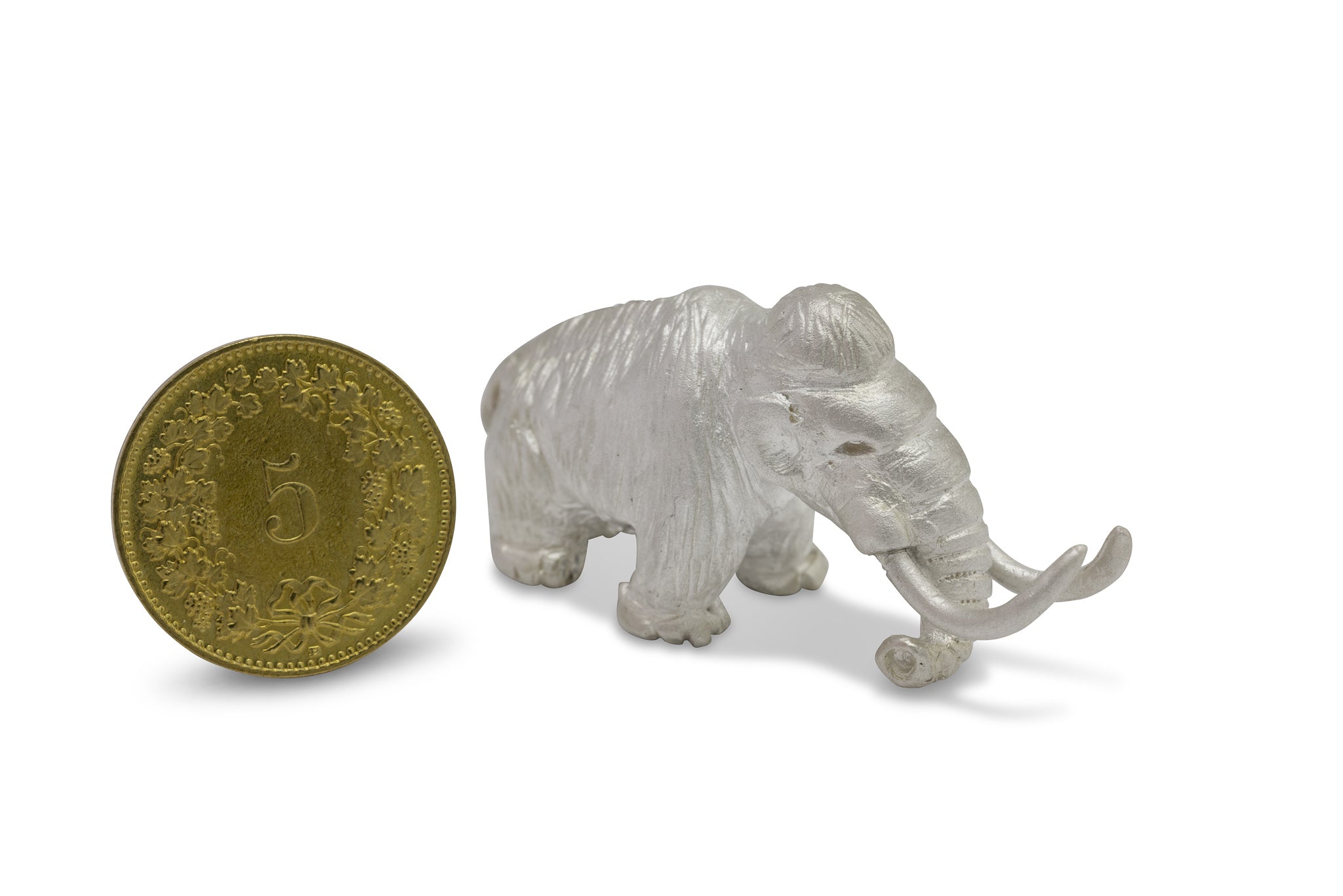 Winziges Mammut aus Silber, das neben 5 Rappen Stück der Schweiz steht. Sie sind nahezu gleich hoch.