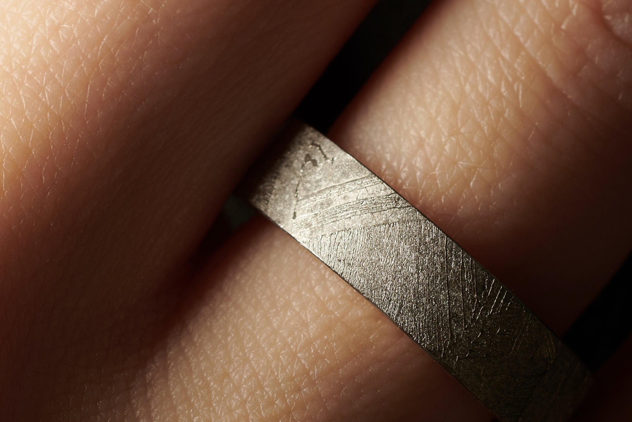 Breiter Ring aus Meteorit mit wunderschönem metallisch glänzenden Widmanstätten Muster. Innenseite aus Gold. Seitlich eckige Kanten. An einer Hand abgebildet